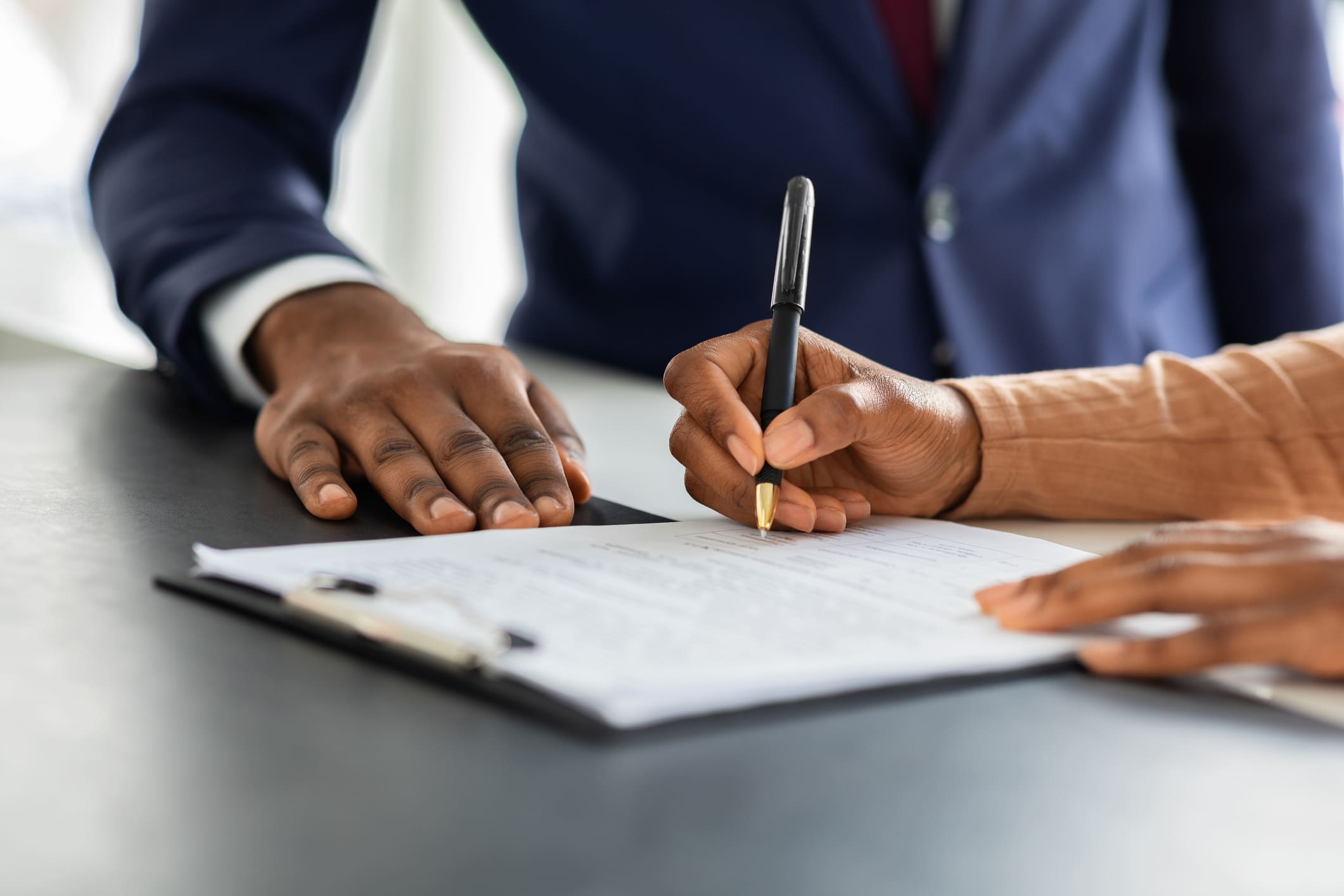 A person signing papers with another person holding a pen.